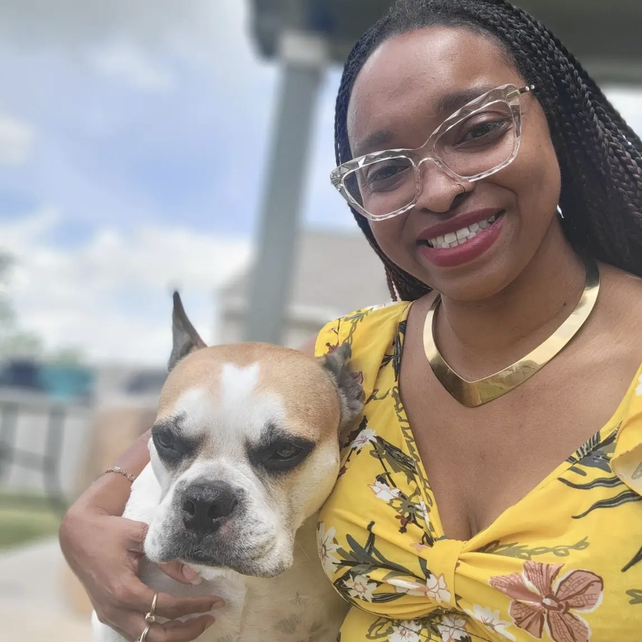 Bre Hart - Owner of You Can Leave Pet Sitting Services in North Austin, Texas Smiling woman in a yellow floral top holding a dog outdoors.